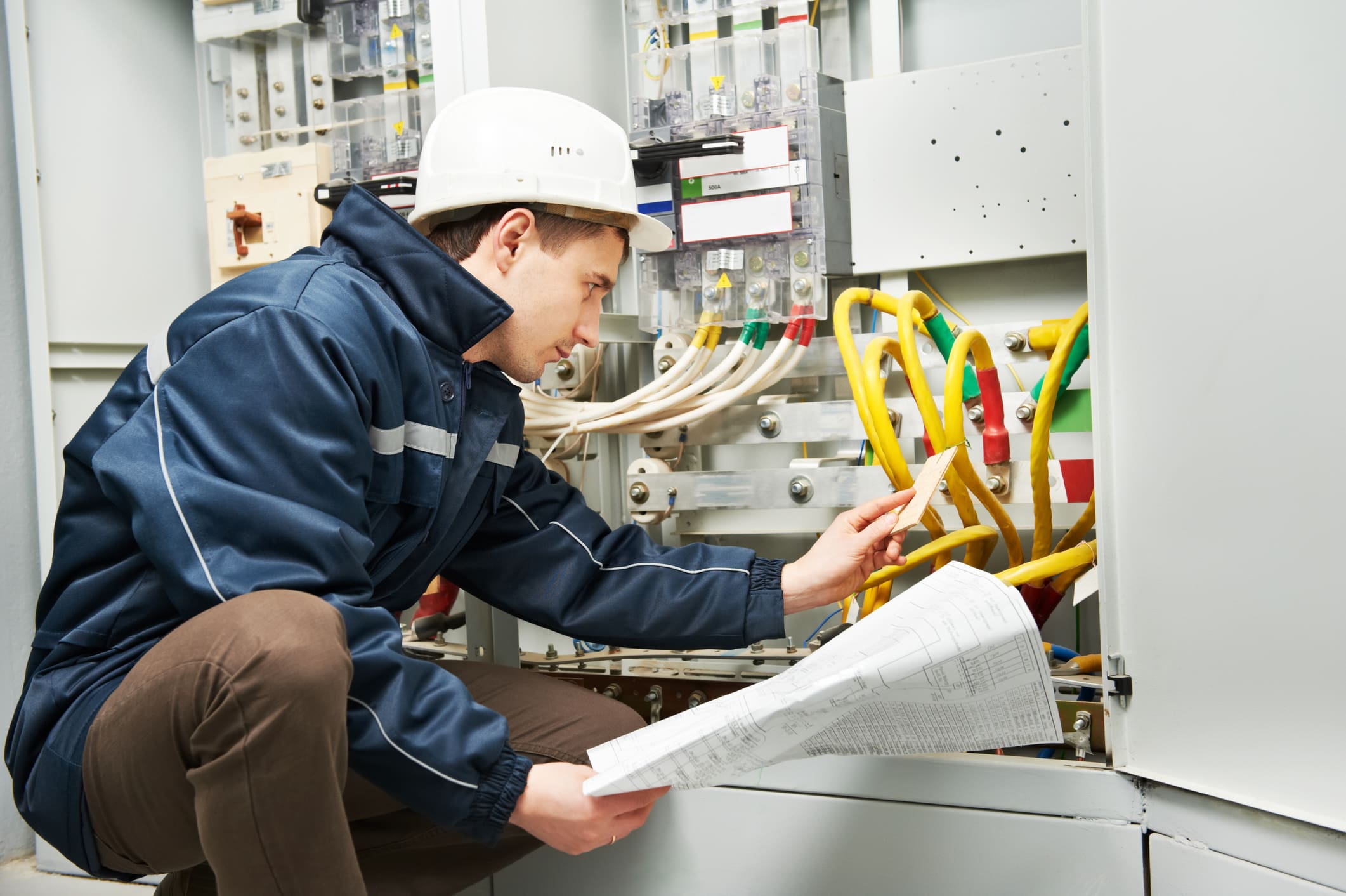 Electrician inspecting control panel with documents.