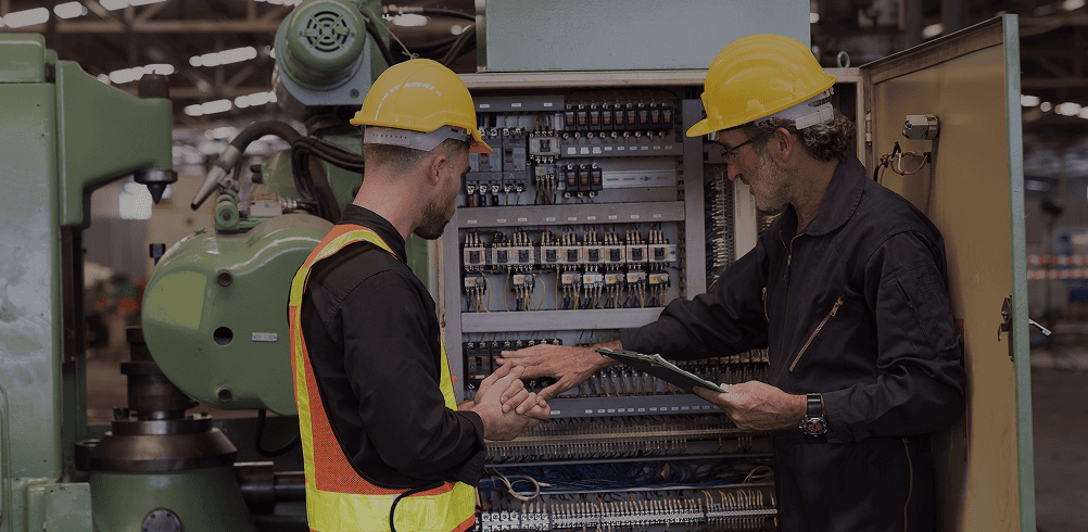 Two workers inspecting industrial machinery controls.
