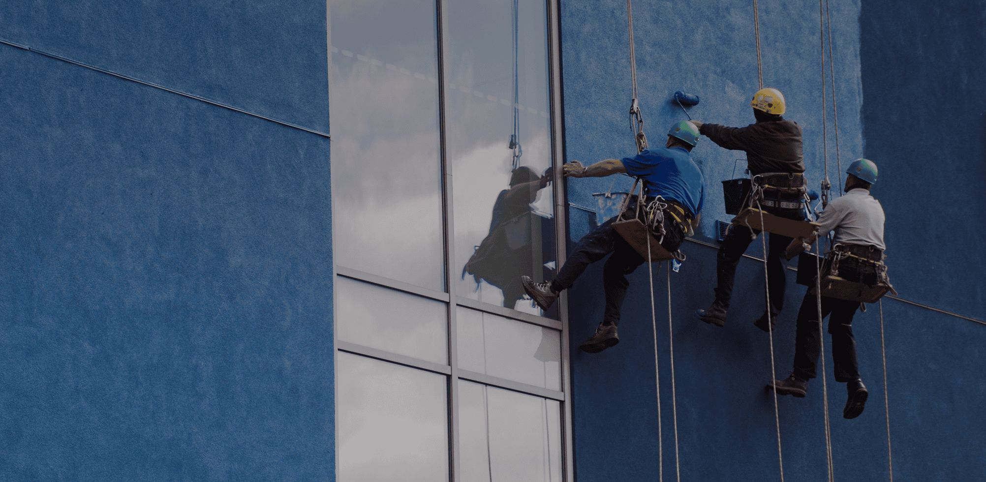 Window cleaners on blue building exterior.