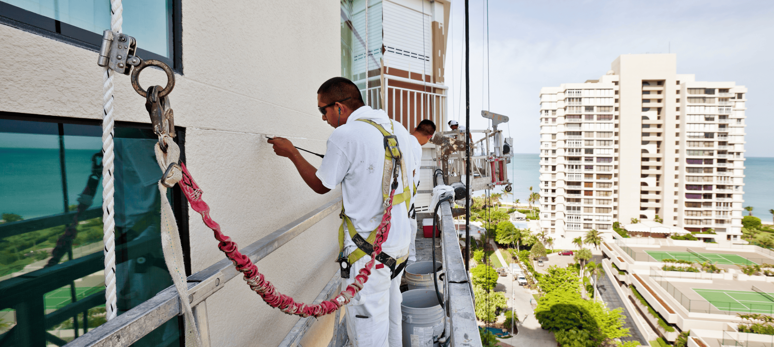 Workers painting high-rise building exterior scaffolding.