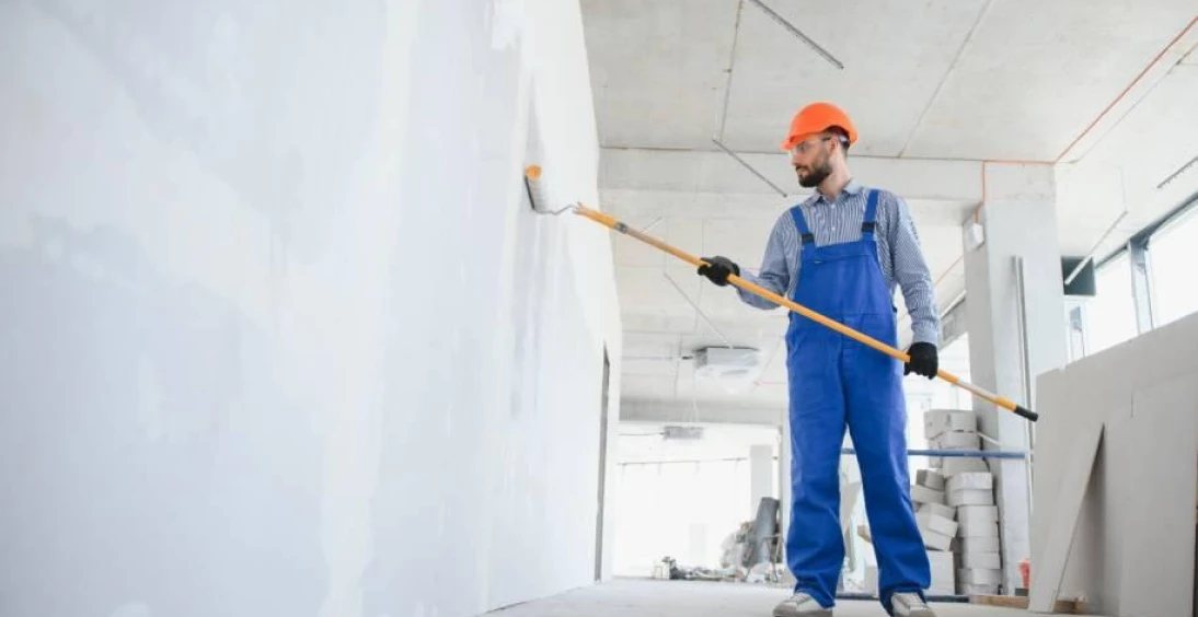 Worker painting wall with roller indoors.